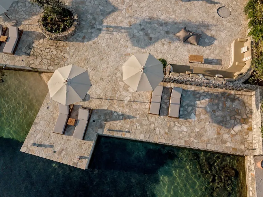 Terrasse der Villa in erster Meereslinie in Luštica, Montenegro: Pool, Liegen, Sonnenschirme und Lounge-Bereich mit Steinverkleidung.
