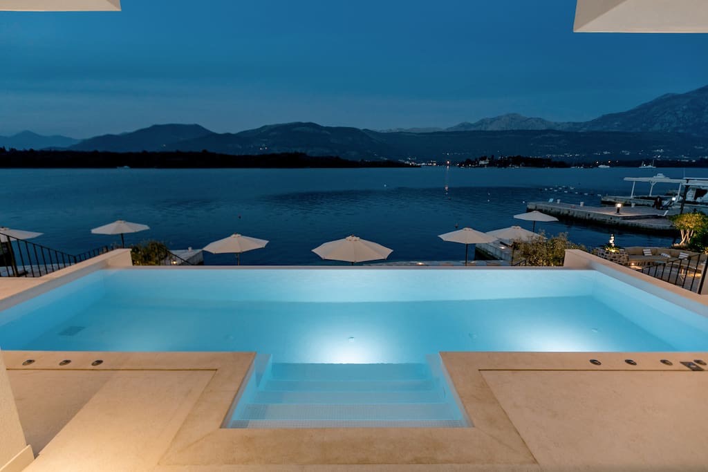 Infinity-Pool mit Beleuchtung in einer Villa in Luštica, Montenegro, mit Panoramablick auf das Meer und die Berge am Abend.