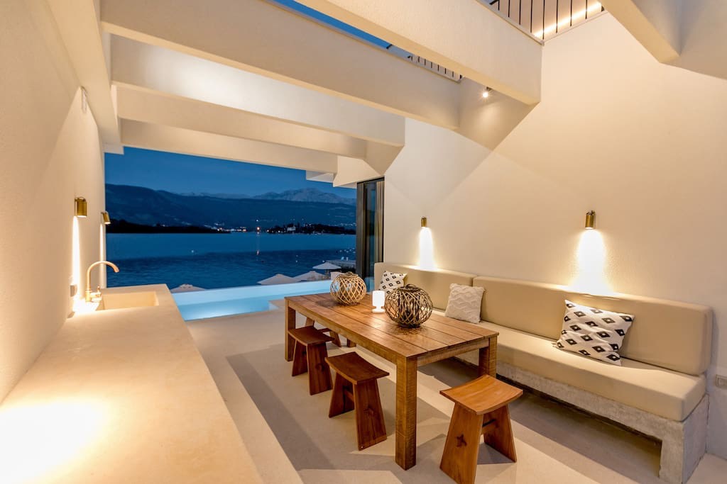 Terrasse der Villa in Luštica, Montenegro: Essbereich mit Holztisch, Meerblick und Pool in erster Meereslinie.