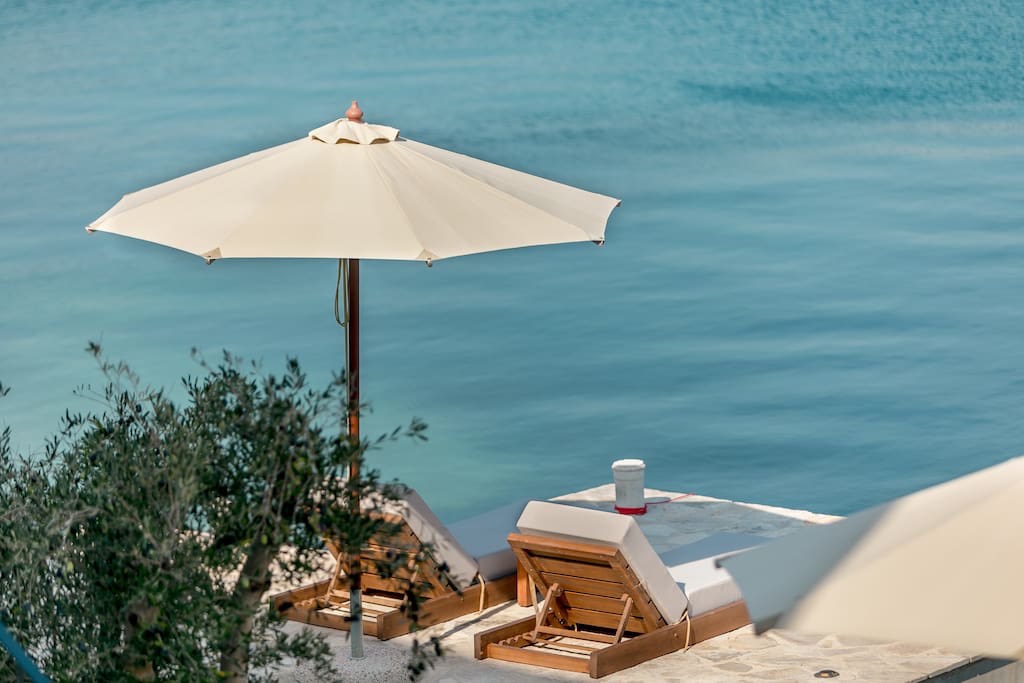 Liegestühle und Sonnenschirm am Privatstrand der Villa in erster Meereslinie in Luštica, Montenegro, mit Blick auf die Adria.