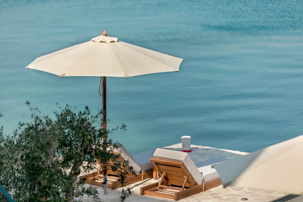 Liegestühle und Sonnenschirm am Privatstrand der Villa in erster Meereslinie in Luštica, Montenegro, mit Blick auf die Adria.