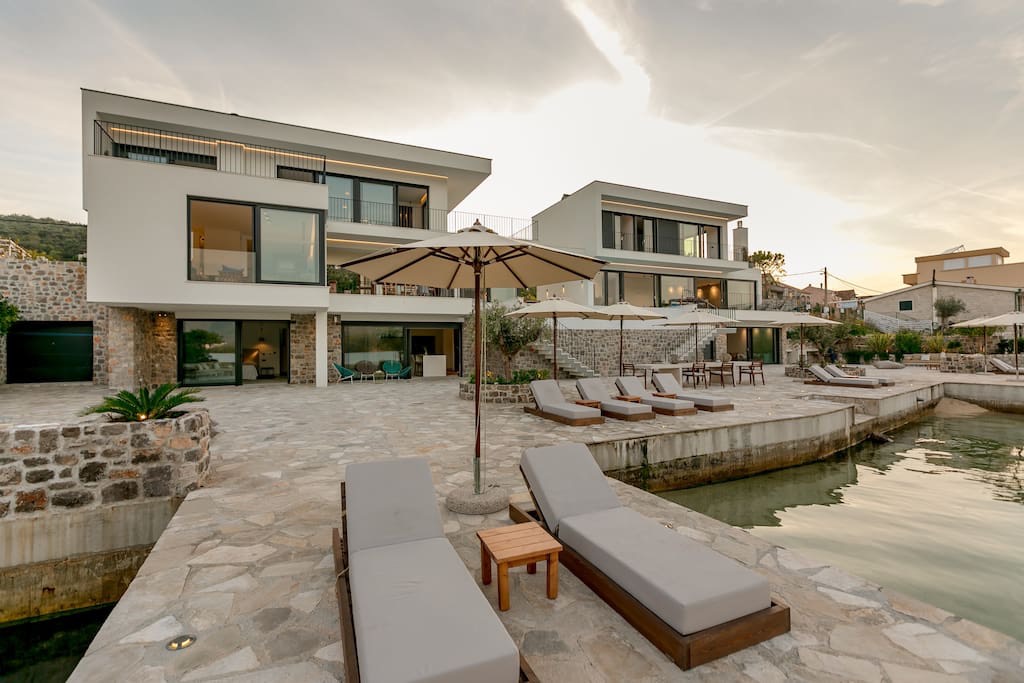 Moderne Villa in erster Meereslinie in Luštica, Montenegro: Terrasse mit Liegestühlen, Steinverkleidung und Zugang zum Meer.