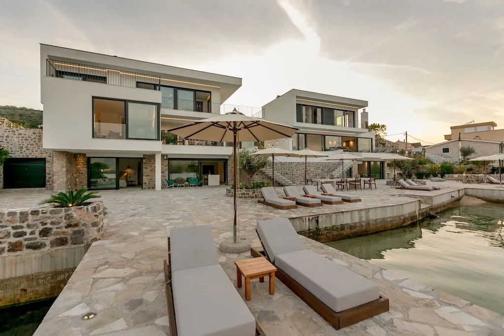 Moderne Villa in erster Meereslinie in Luštica, Montenegro: Terrasse mit Liegestühlen, Steinverkleidung und Zugang zum Meer.