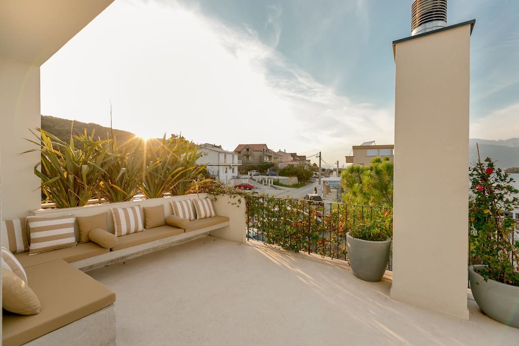 Geräumige Terrasse der Villa in Luštica, Montenegro: eingebaute Möbel mit Kissen, Pflanzen und Blick auf die Küste.