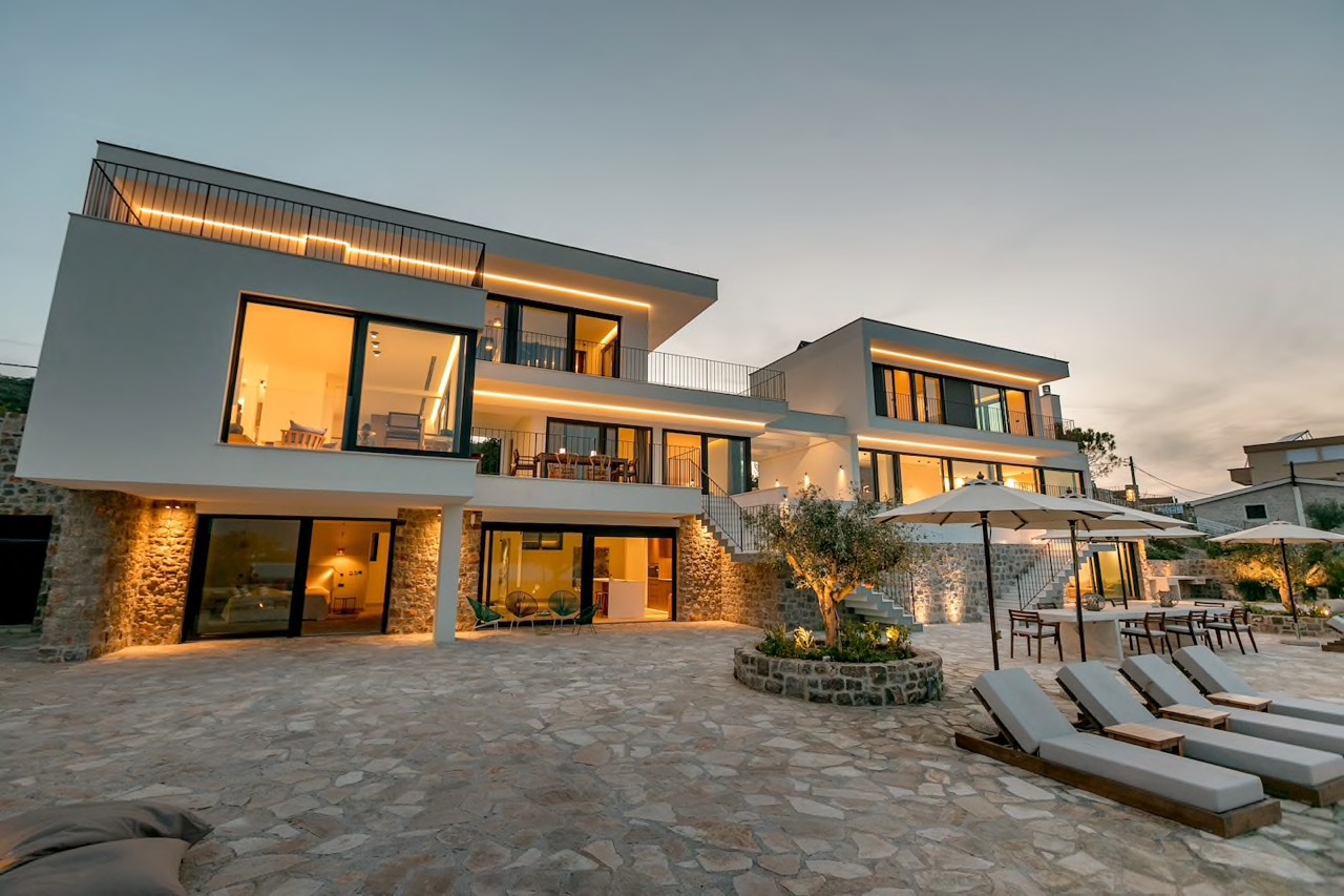 Moderne Villa in Luštica, Montenegro: Panoramafenster, Terrasse mit Liegen, Steinverkleidung und Abendbeleuchtung.