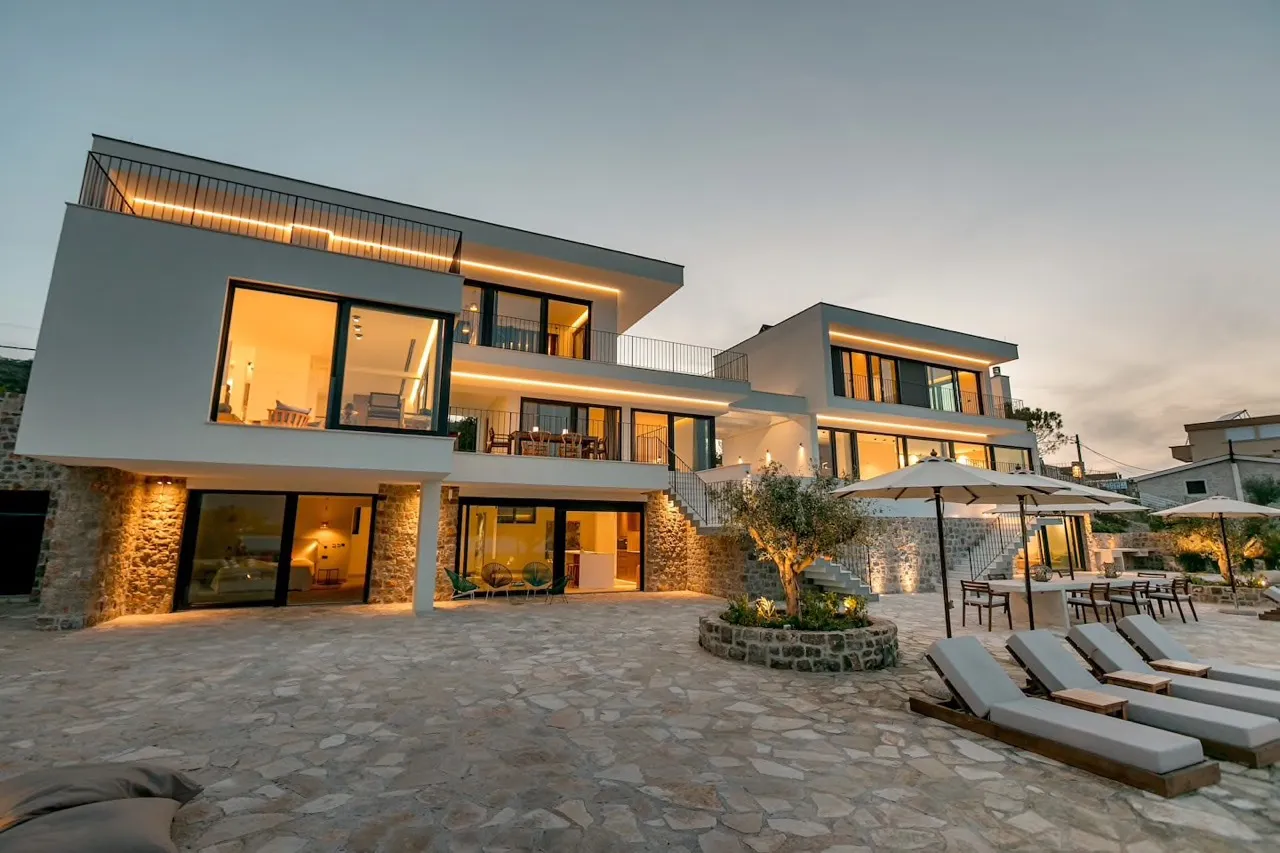 Moderne Villa in Luštica, Montenegro: Panoramafenster, Terrasse mit Liegen, Steinverkleidung und Abendbeleuchtung.
