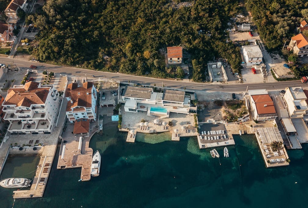 Luftaufnahme einer Villa in erster Meereslinie in Luštica, Montenegro: Privatstrand, Pool, Steg und Yachten am Meer.