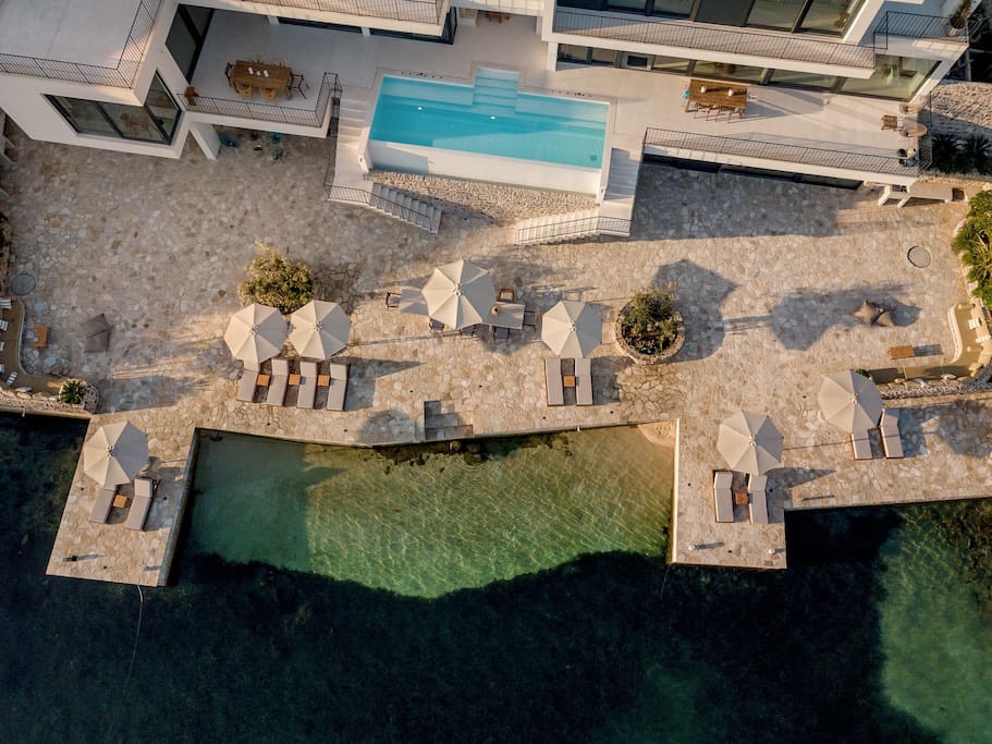 Blick von oben auf eine Luxusvilla in Luštica, Montenegro: Pool, Terrasse mit Liegestühlen und direkter Zugang zum Meer.
