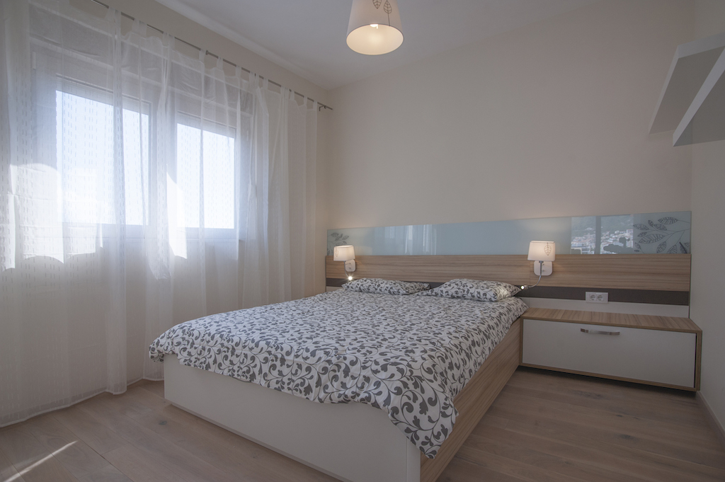 Helles Schlafzimmer mit Doppelbett in einer Wohnung in Budva, Montenegro: moderne Möbel und Blick aus dem Fenster.