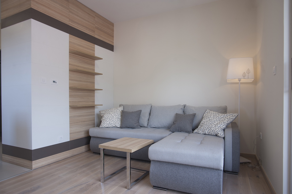 Modernes Wohnzimmer in einer Wohnung in Budva, Montenegro: graues Ecksofa, Holztisch und Regal.