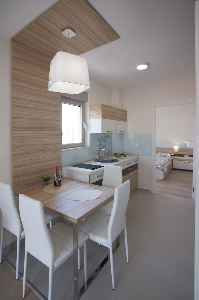 Moderne Wohnküche in einer Wohnung in Budva, Montenegro: helle Möbel, Essbereich und Blick auf das Schlafzimmer.