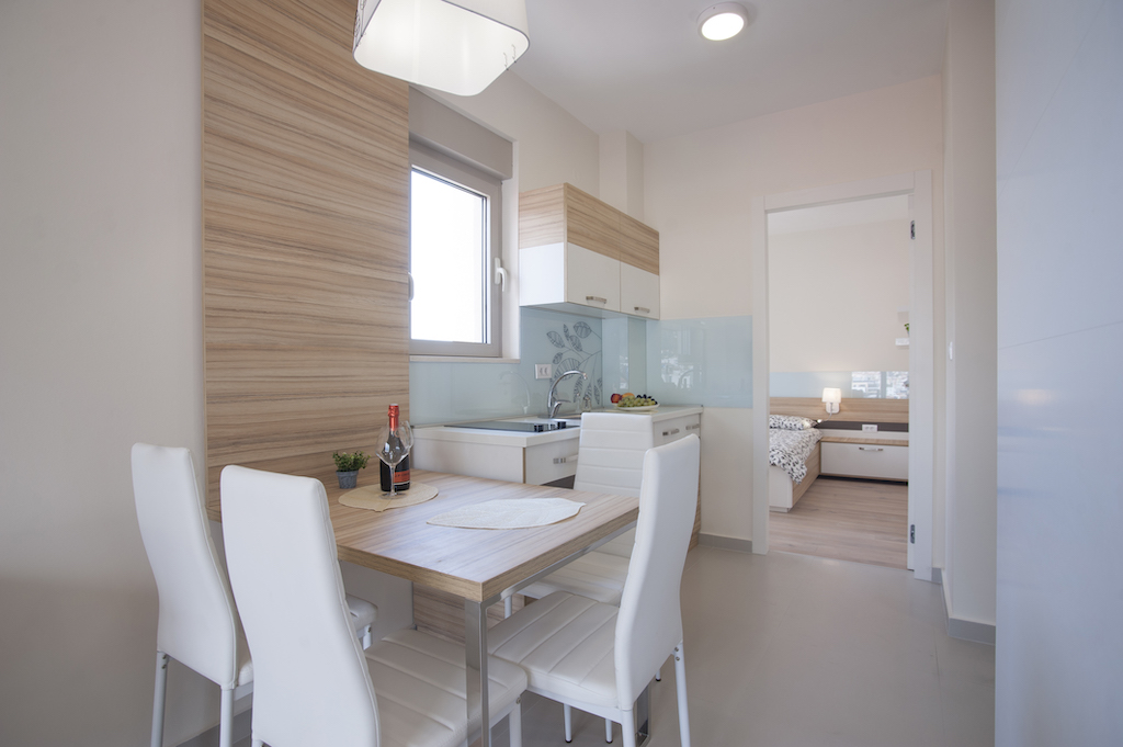 Moderne Wohnküche in einer Wohnung in Budva, Montenegro: helle Möbel, Essbereich und Blick ins Schlafzimmer.