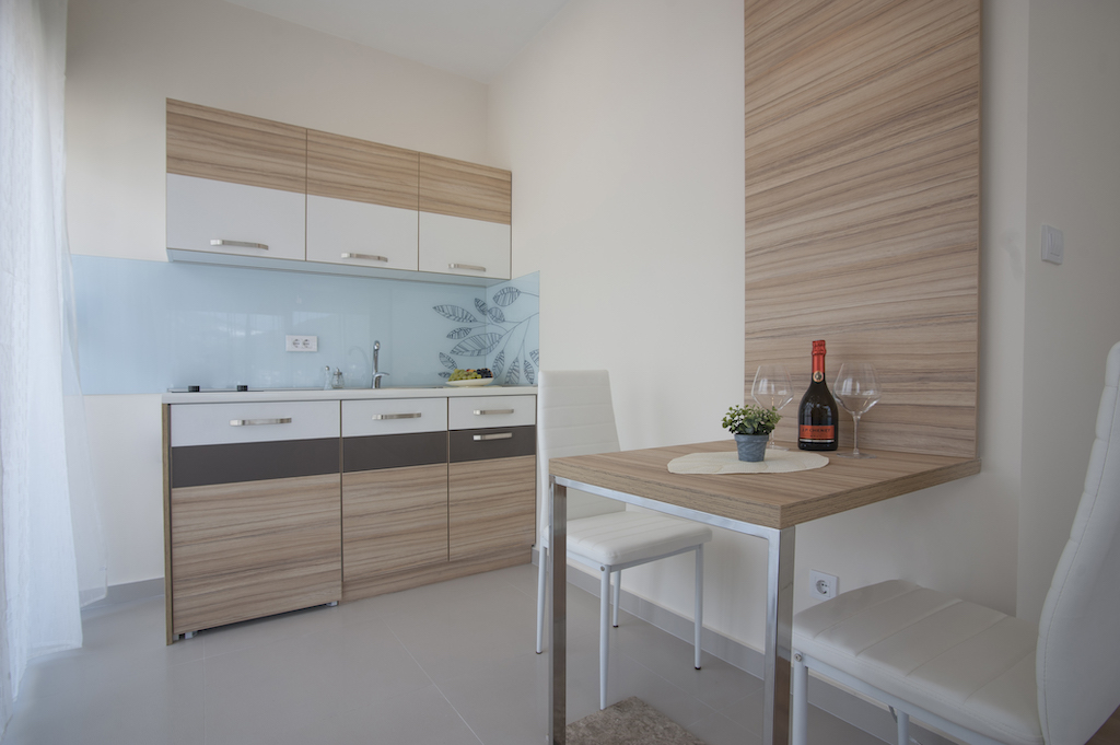 Moderne Küche in einer Wohnung in Budva, Montenegro: helle Einbauküche, Essbereich und stilvolle Holzverkleidung.