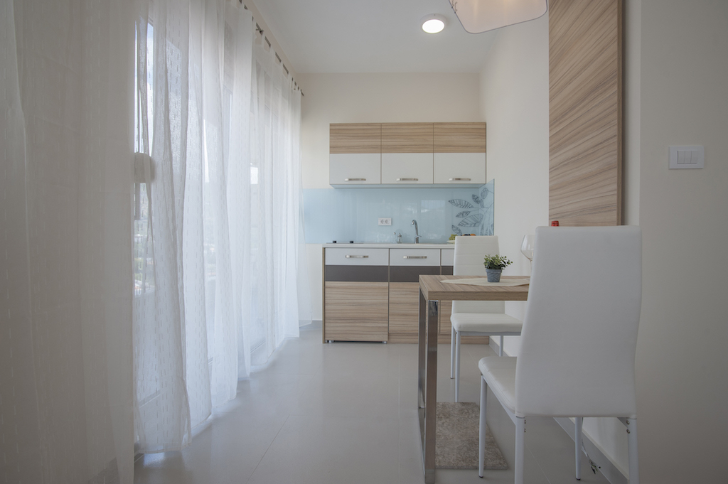 Moderne Wohnküche in einer Wohnung in Budva, Montenegro: helle Einbauküche, Essbereich und Panoramafenster.