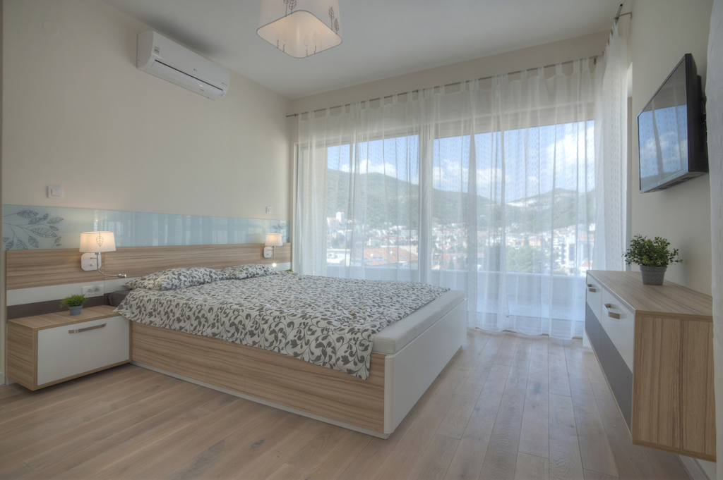 Modernes Schlafzimmer in einer Wohnung in Budva, Montenegro: Doppelbett, Panoramafenster mit Blick auf die Berge und die Stadt.