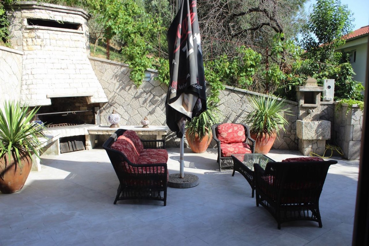Terrasse der Villa in Budva, Montenegro: Ruhebereich mit geflochtenen Möbeln, Steingrill und Garten im mediterranen Stil.