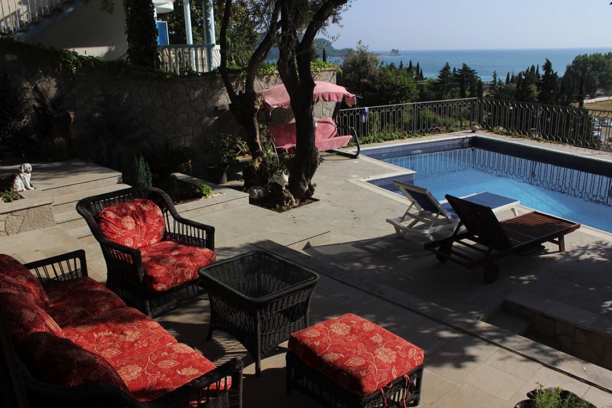 Terrasse der Villa in Budva, Montenegro: Pool, Rattanmöbel mit roten Kissen und Panoramablick auf das Meer.