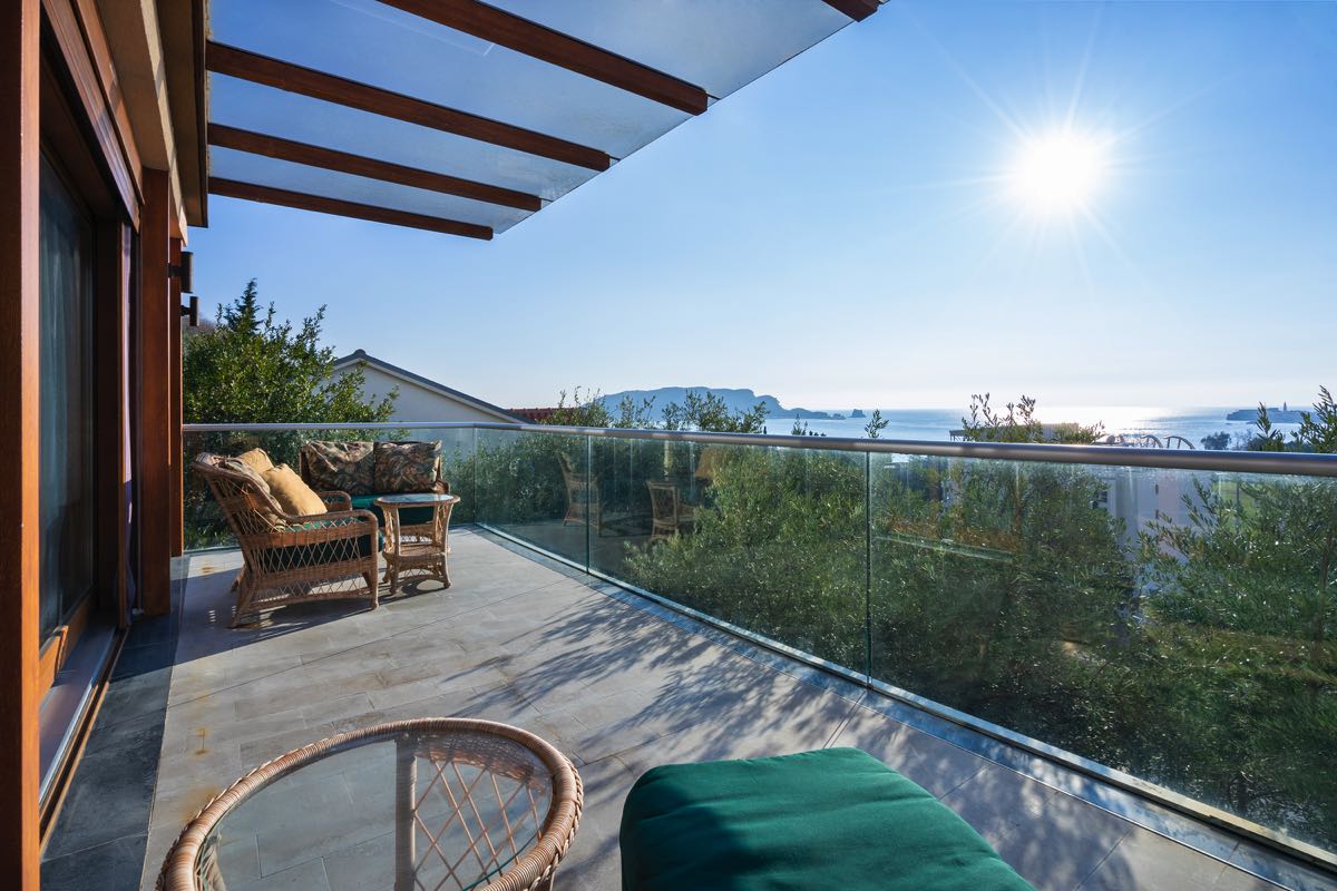 Geräumige Terrasse einer Villa in Budva, Montenegro, mit Rattanmöbeln, Glasgeländer und Panoramablick auf das Meer.