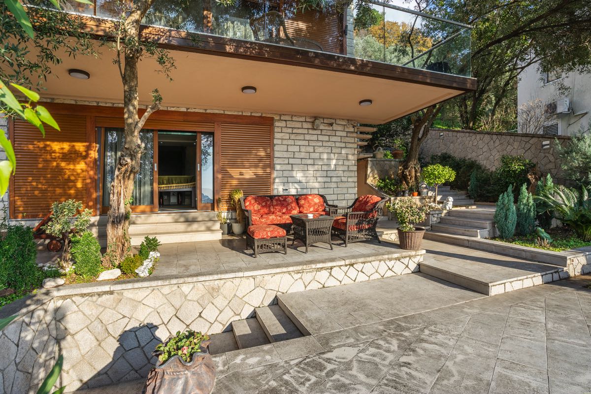 Terrasse einer Villa in Budva, Montenegro: Steinverkleidung, geflochtene Möbel mit roten Kissen und Landschaftsgestaltung.
