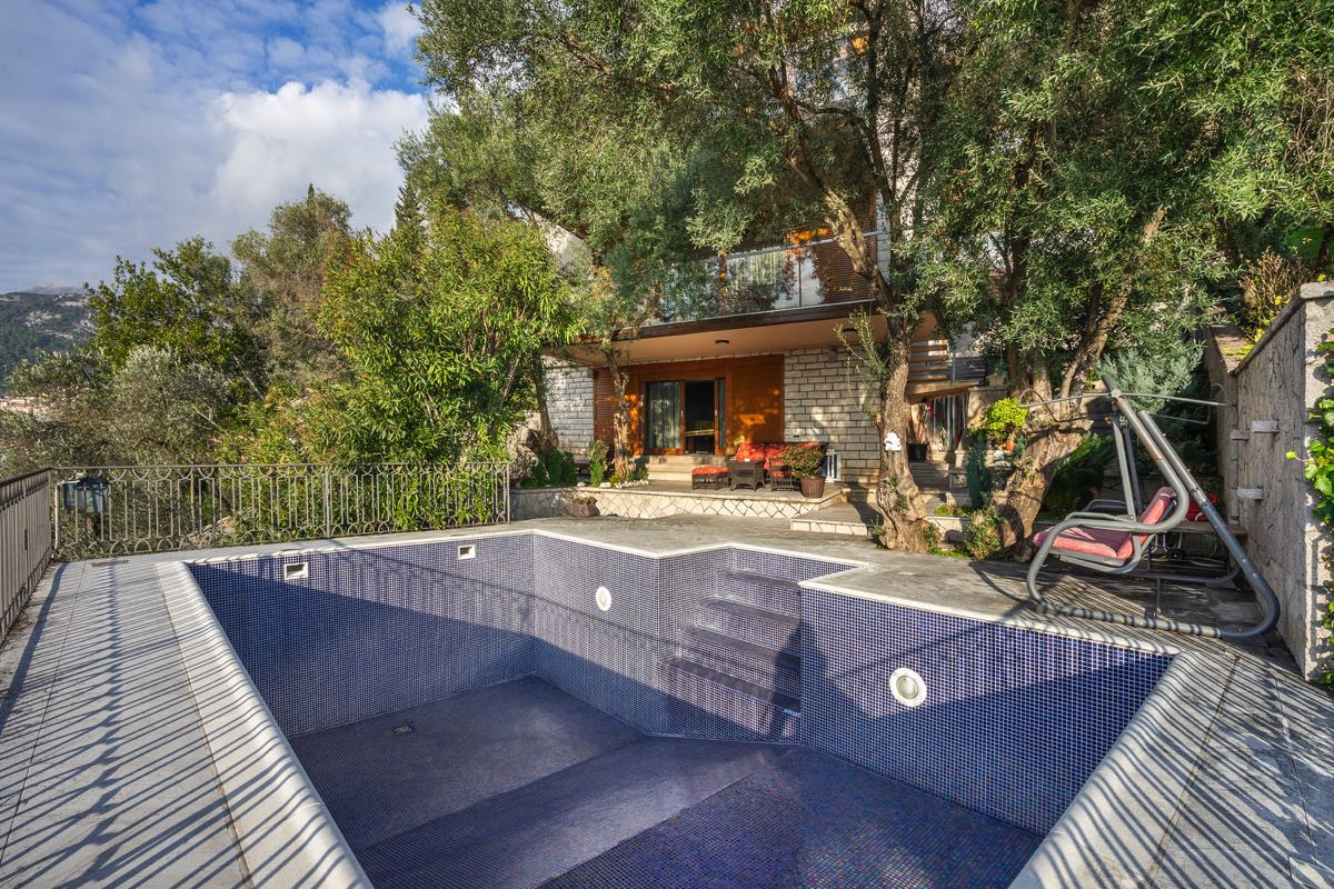 Privater Pool mit Mosaikverkleidung und Terrasse mit Schaukel an der Villa in Budva, Montenegro, umgeben von Olivenbäumen.