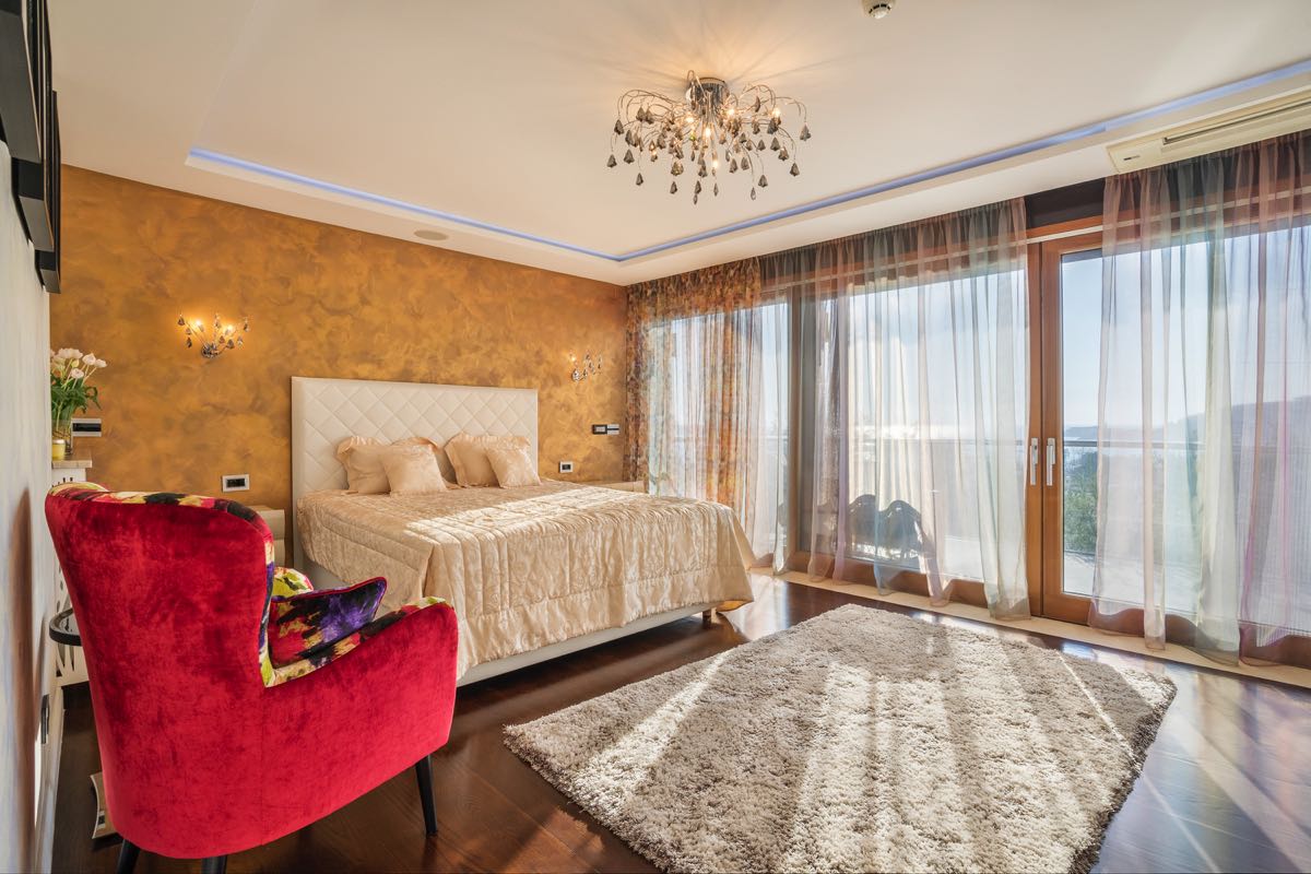 Schlafzimmer mit Doppelbett, rotem Sessel und Panoramafenstern in einer Villa in Budva, Montenegro.