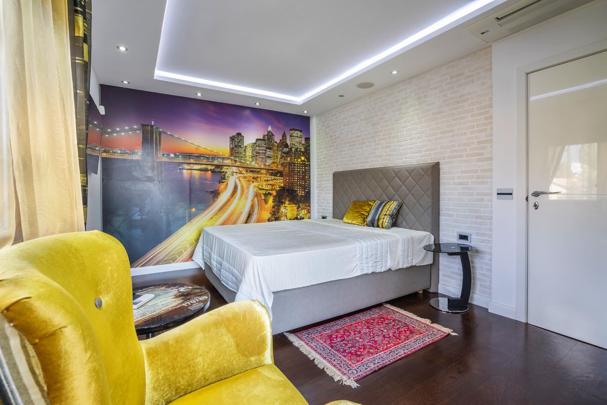 Modernes Schlafzimmer in einer Villa in Budva, Montenegro: Doppelbett, Fototapete mit Stadtmotiv, gelber Sessel und Dekor.