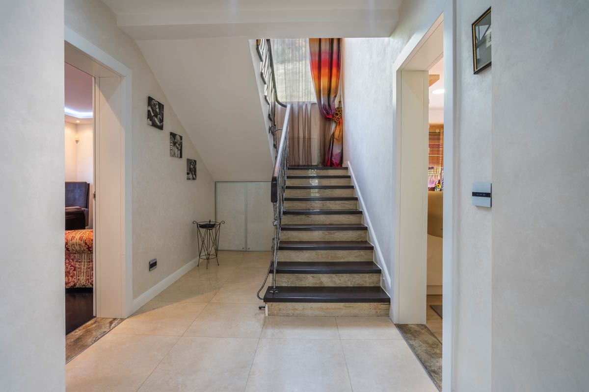 Innenraum einer Villa in Budva, Montenegro: heller Flur mit Treppe aus dunklem Holz und schmiedeeisernem Geländer.