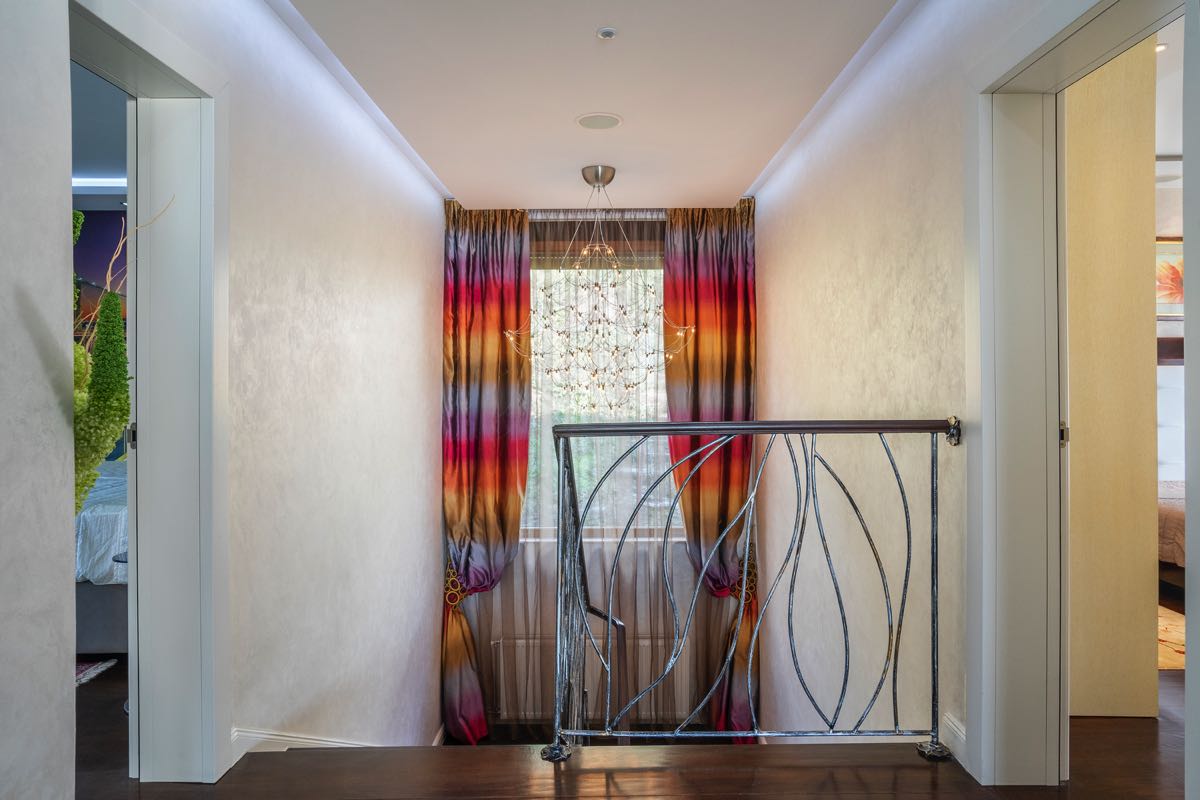 Innenraum einer Villa in Budva, Montenegro: Treppenhalle mit Designer-Vorhängen, schmiedeeisernem Geländer und Kronleuchter.