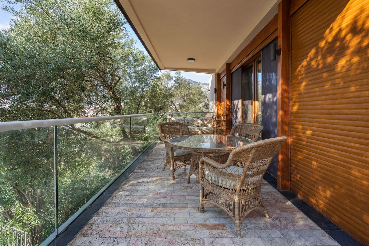 Gemütlicher Balkon mit Rattanmöbeln und Blick ins Grüne in einer Villa in Budva, Montenegro: Terrasse mit Steinboden und Geländer.