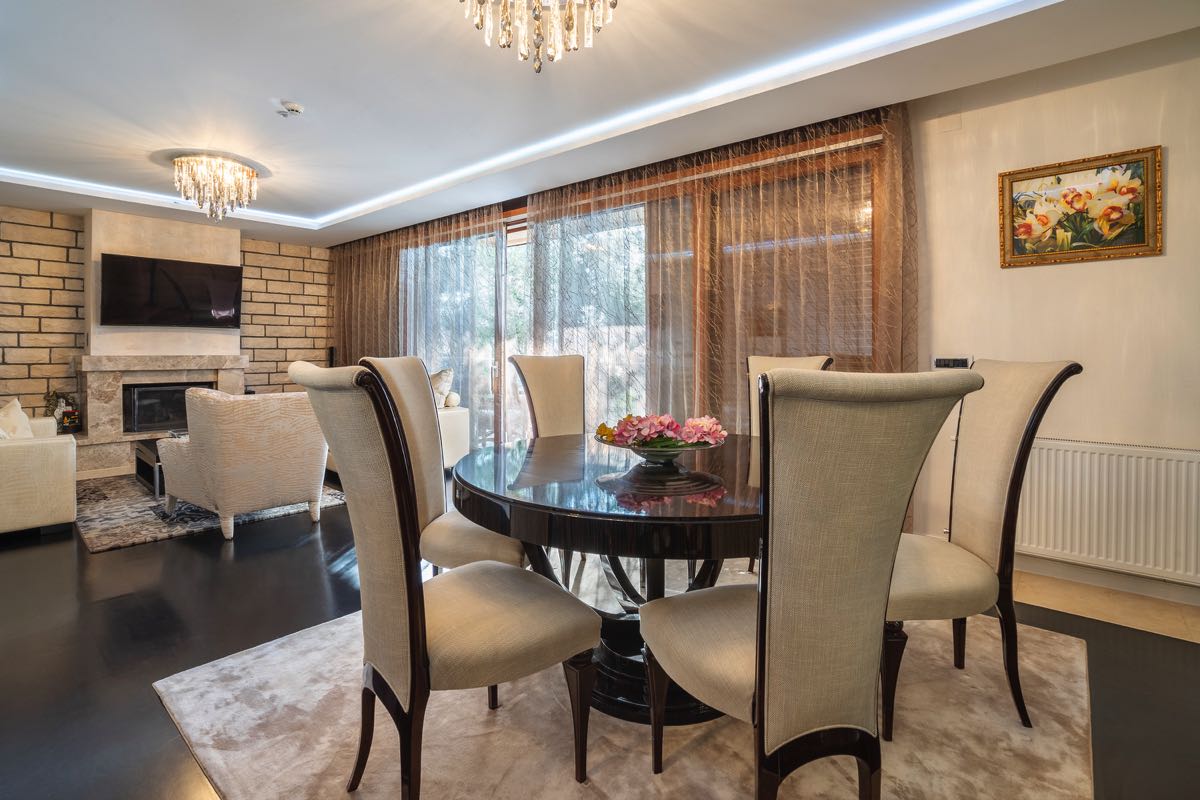 Wohnzimmer mit Essbereich und Kamin in einer Villa in Budva, Montenegro: modernes Interieur, dunkler Boden und Kronleuchter.