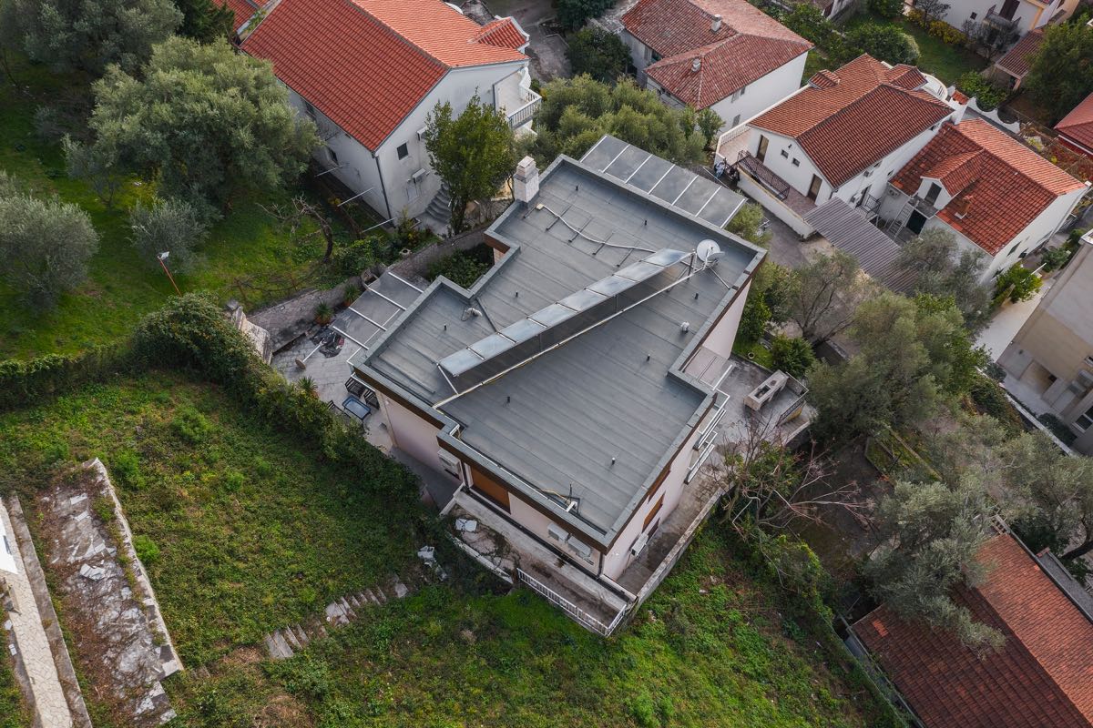 Luftaufnahme einer Villa in Budva, Montenegro: Flachdach mit Solarpaneelen, Terrasse und grüne Umgebung.