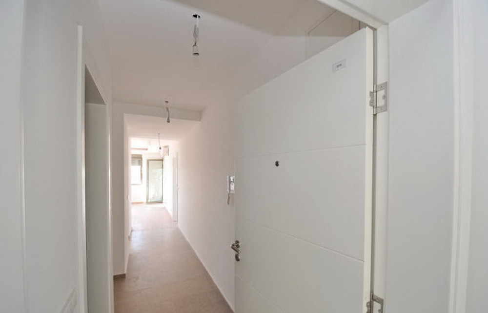 Heller Flur in einer neuen Wohnung in einer Wohnanlage in Tivat, Montenegro: weiße Wände, Eingangstür und Fliesenboden.