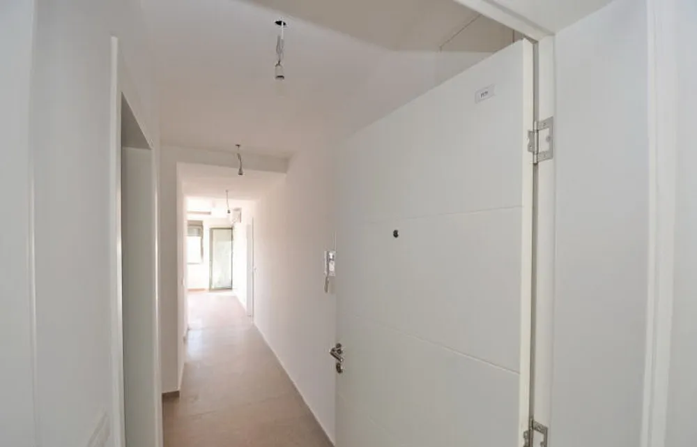 Svetao hodnik u novom stanu u stambenom kompleksu u Tivtu, Crna Gora: beli zidovi, ulazna vrata i pločice na podu.