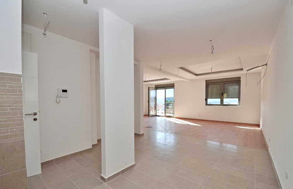 Geräumiges Wohnzimmer mit Ausstattung in einem Neubau in Tivat, Montenegro: helle Wände, Fliesenboden und Meerblick.
