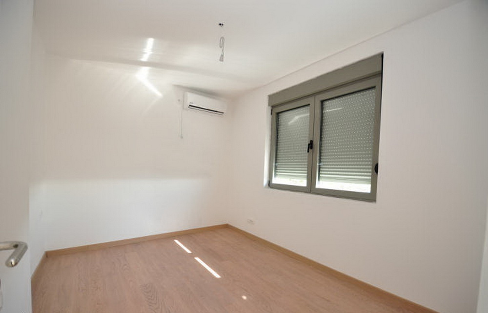 Helles Schlafzimmer in einem Neubau in Tivat, Montenegro: Laminat, weiße Wände, Klimaanlage und Fenster mit Rollläden.