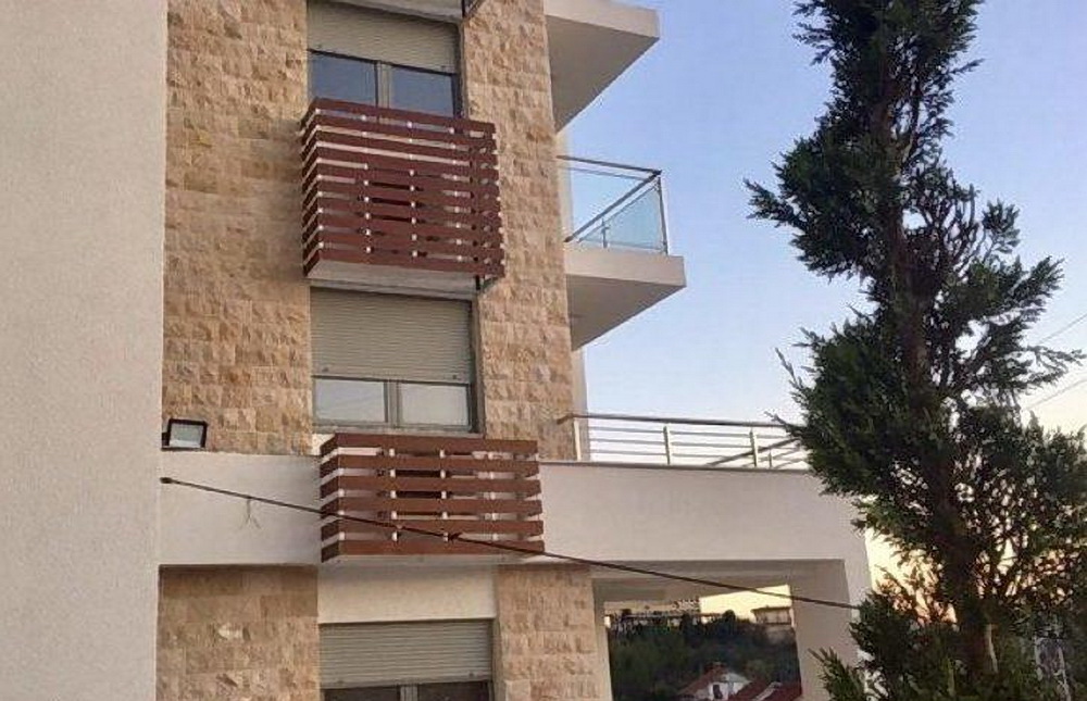 Fassade eines modernen Wohnkomplexes in Tivat, Montenegro: Steinverkleidung, Balkone mit Holzelementen und Rollläden.