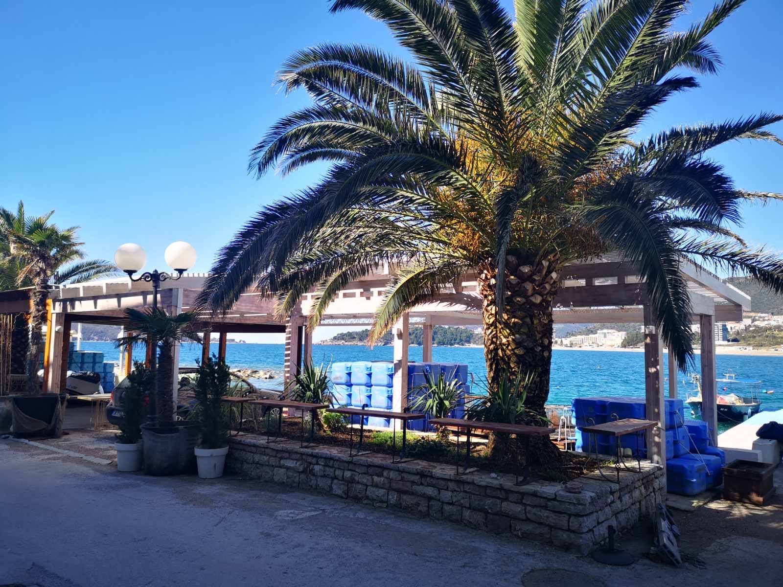 Local commercial en première ligne de mer à Rafailovici, Monténégro : terrasse avec palmiers et vue sur la plage.