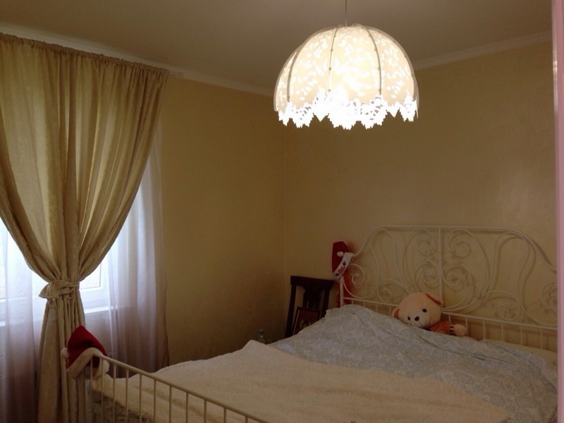 Chambre cosy avec lit en fer forgé et luminaire ajouré dans une villa à Šušanj, Monténégro. Tons clairs, style classique.