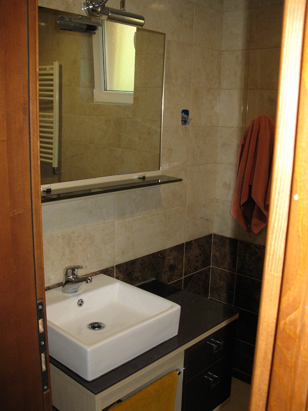 Salle de bains dans une villa à Šušanj, Monténégro : lavabo moderne, miroir et finitions en carrelage dans des tons clairs.