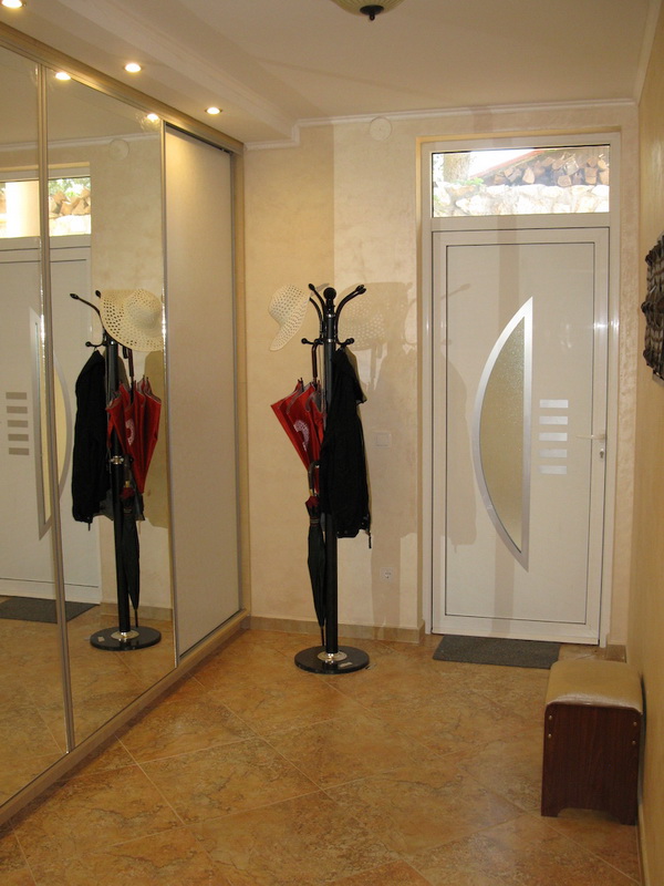 Entrée de la villa à Shushan, Monténégro : placard coulissant miroir, porte-manteau sur pied, finitions claires et sol carrelé.