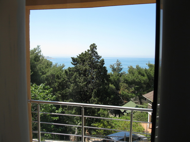 Vue depuis le balcon de la villa à Shushan, Monténégro : panorama sur la mer, la forêt de conifères et le jardin verdoyant avec une clôture moderne.