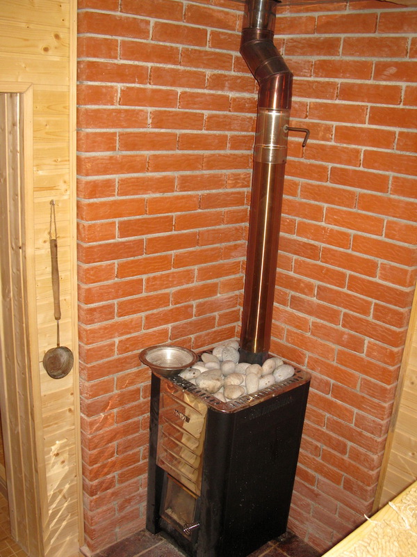 Poêle Harvia avec pierres dans le sauna de la villa à Šušanj, Monténégro, finition des murs en brique rouge et bois clair.
