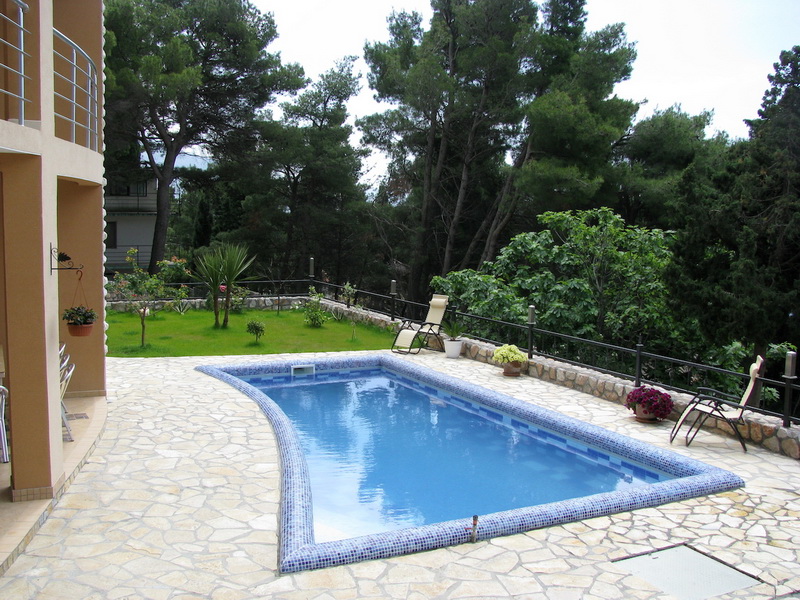 Piscine privée dans une villa à Šušanj, Monténégro : terrasse en pierre, chaises longues et jardin verdoyant autour.