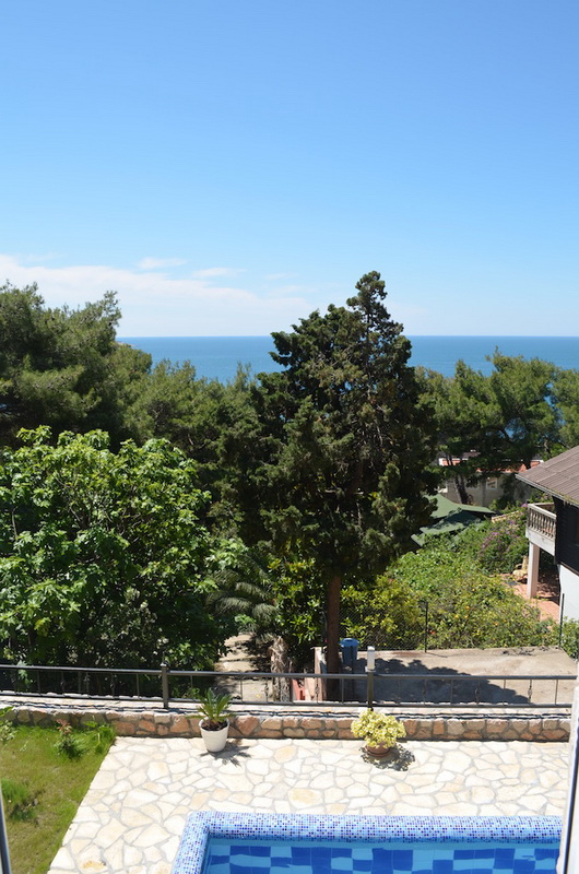 Vue sur la mer et le jardin depuis la terrasse de la villa avec piscine à Šušanj, Monténégro : finition en pierre, conifères et ciel bleu.