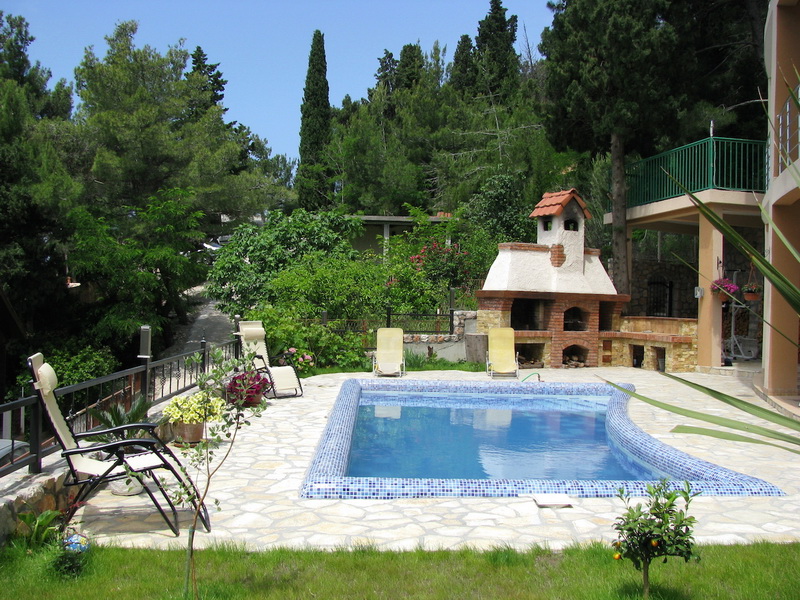 Piscine avec espace détente et barbecue dans une villa à Shushan, Monténégro : terrasse en pierre, chaises longues et jardin avec conifères.