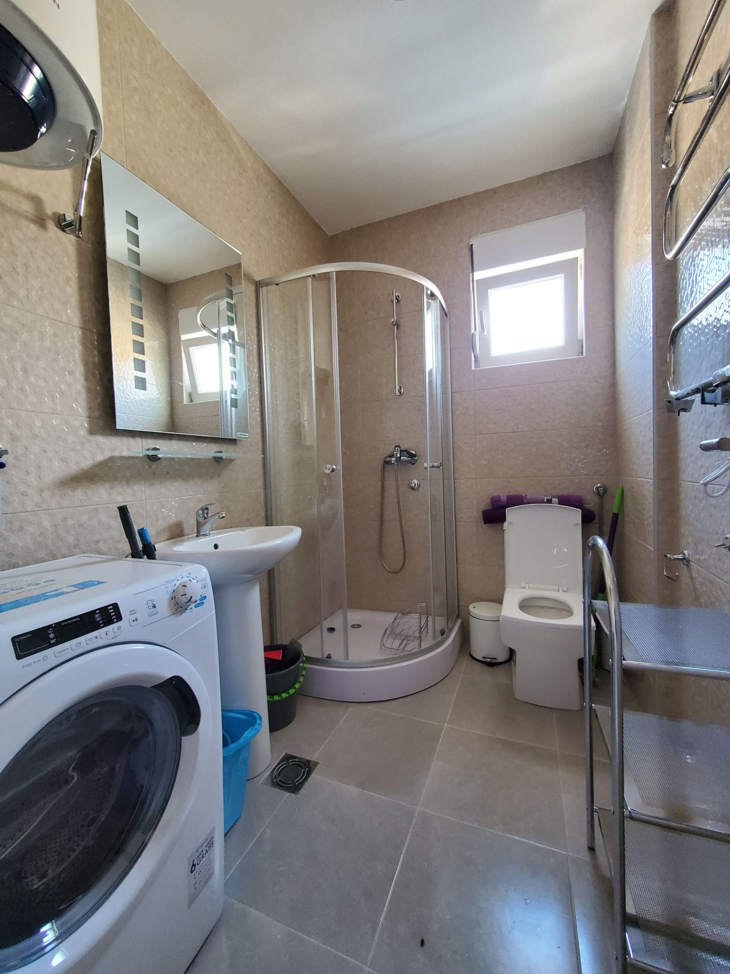 Badezimmer in einer Wohnung in Budva, Montenegro: Duschkabine, Waschmaschine, Waschbecken und helle Fliesen.