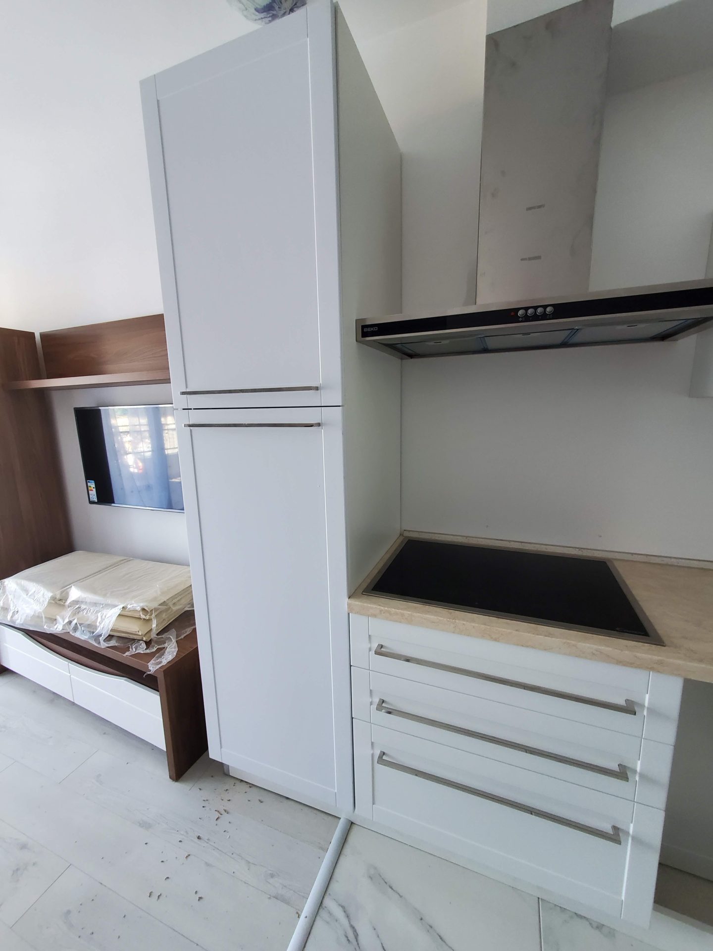 Moderne Küche in einer Wohnung in Budva, Montenegro: weiße Fronten, integrierte Geräte und TV-Bereich in hellem Interieur.