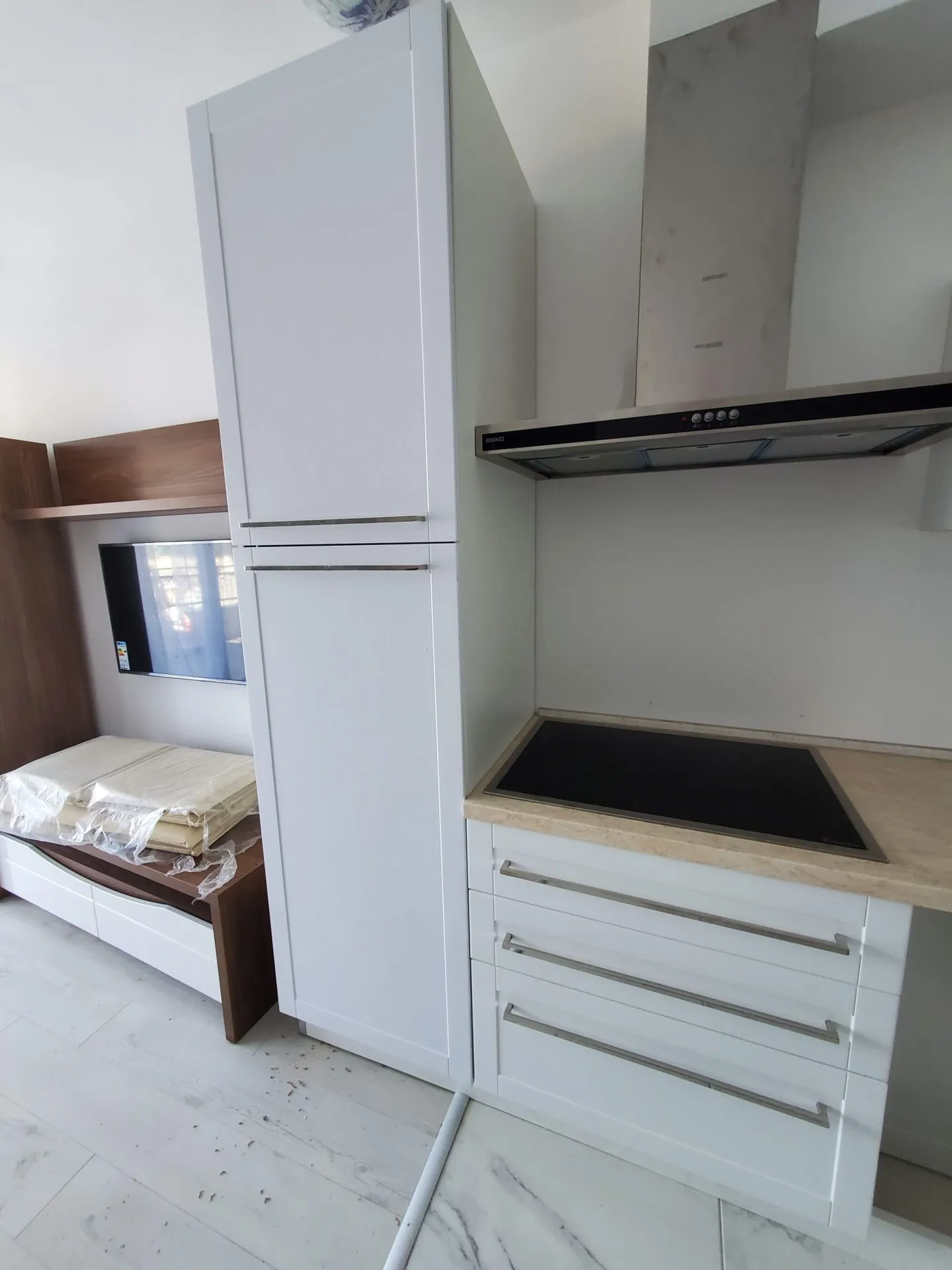 Moderne Küche in einer Wohnung in Budva, Montenegro: weiße Fronten, integrierte Geräte und TV-Bereich in hellem Interieur.