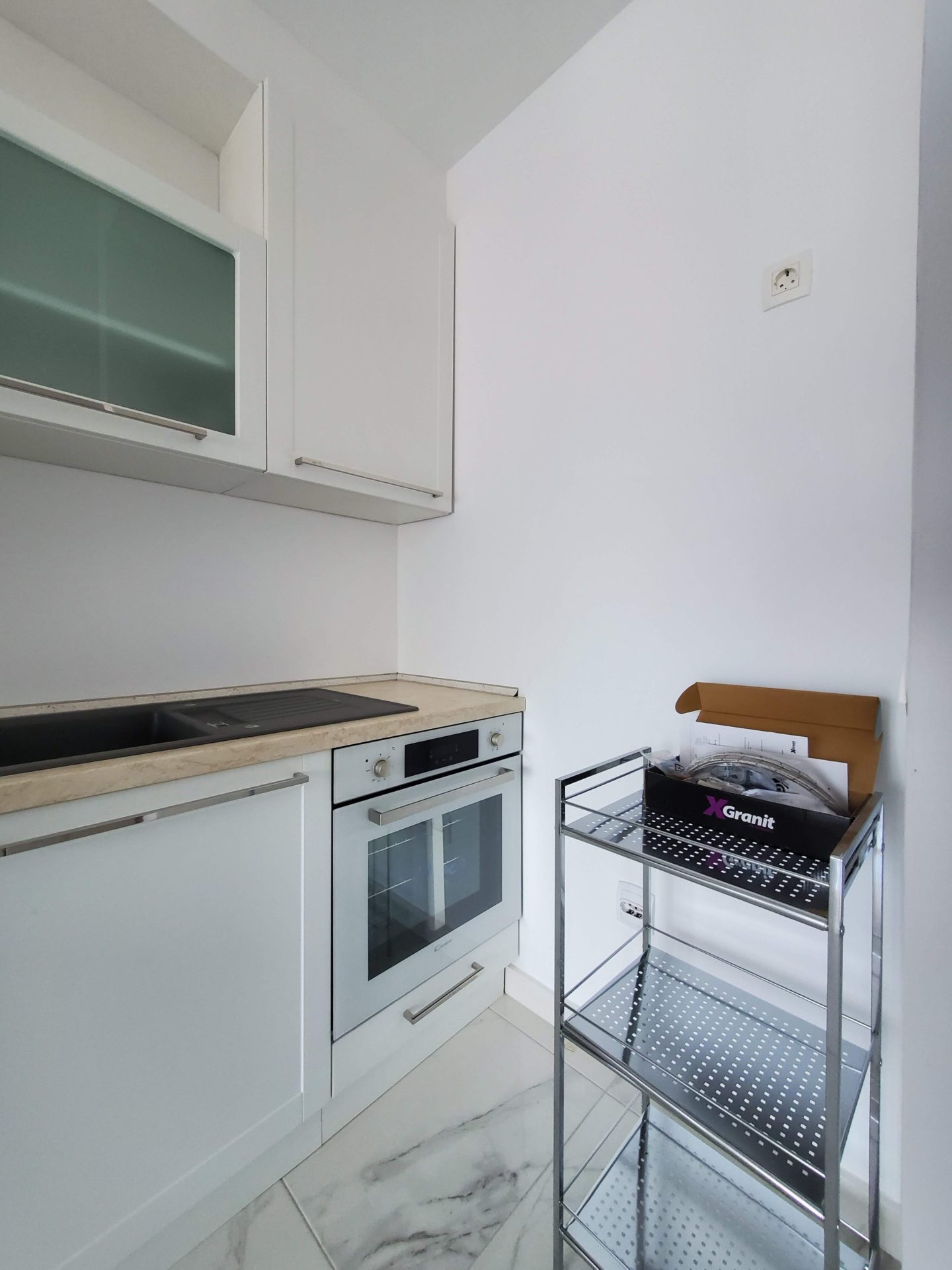 Moderne weiße Küche mit Geräten in einer Wohnung in Budva, Montenegro: Einbauofen und Steinspüle.