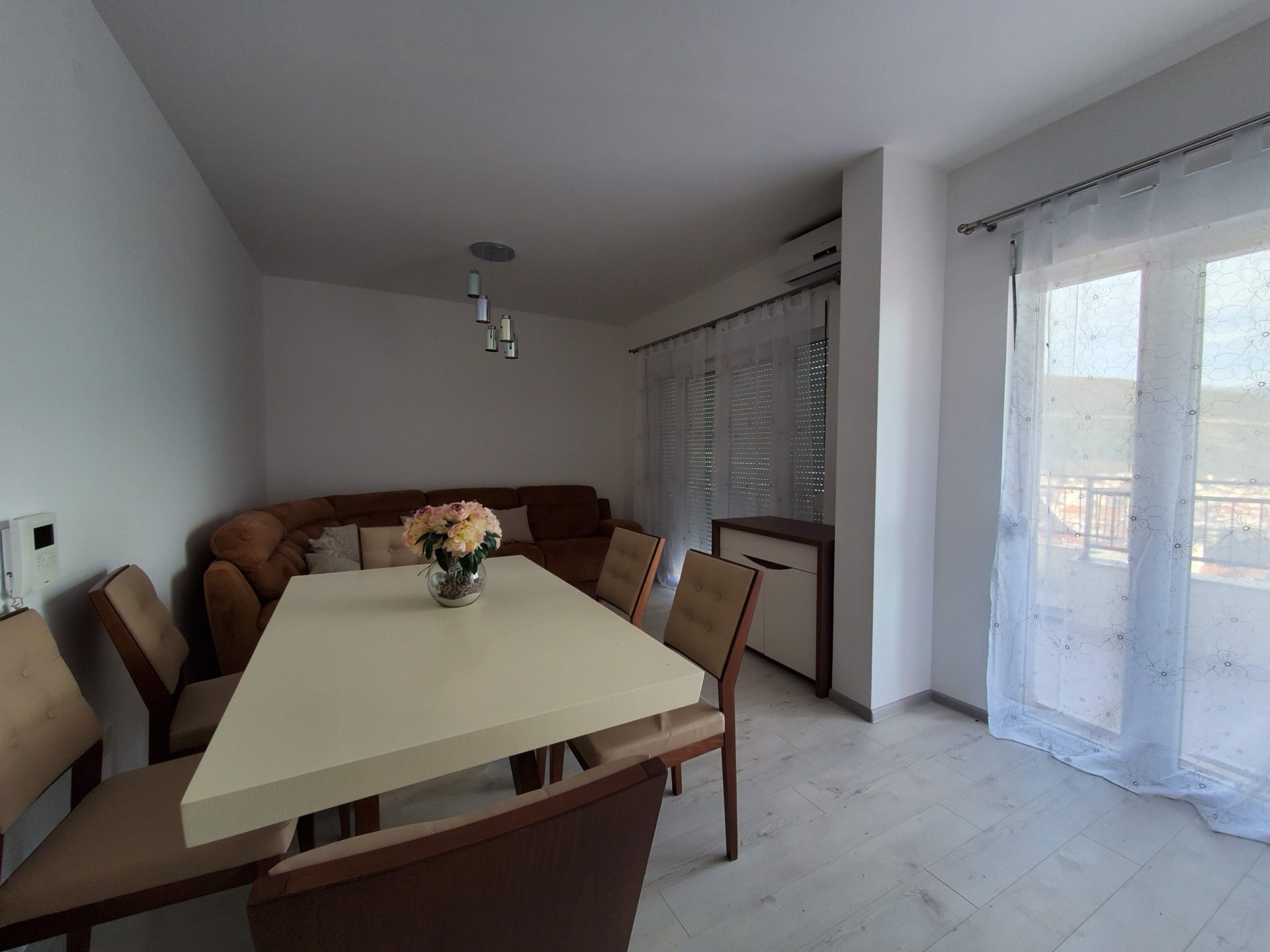 Helles Wohnzimmer mit Essbereich und weichem Sofa in einer Wohnung in Budva, Montenegro. Modernes Interieur mit Zugang zum Balkon.